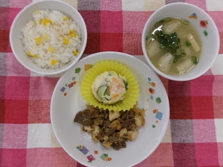 今日の給食のとうもろこしご飯、牛肉と糸こんの炒り煮、ポテトサラダ、玉ねぎのみそ汁が盛り付けられている様子。