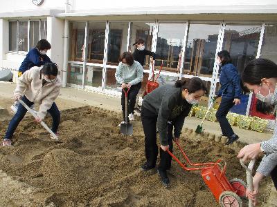 砂場に砂を入れる職員