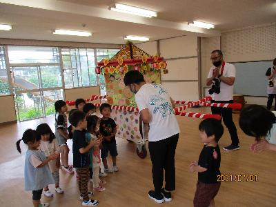 せみ組のお友達が、保育者から開園記念日におみこしを担ぐ由来を聞いている画像