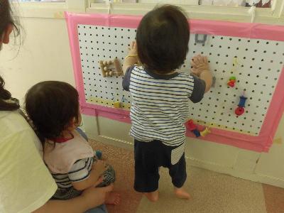 0歳児が壁に貼り付けた指先遊びのおもちゃで遊んでいる様子