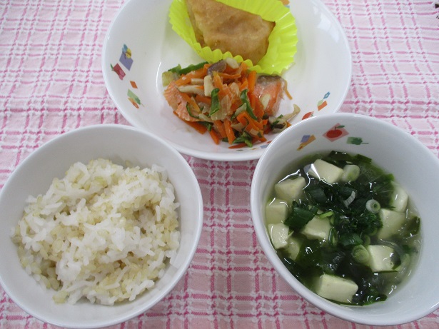 お皿に盛りつけられた給食・玄米ご飯・鮭のちゃんちゃん焼き・五目スープ・柿とりんごの春巻き