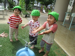 スプリンクラー前に並んで水が出ることを待っている1歳児