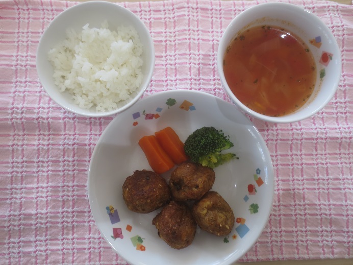 今日の給食、白ご飯、いわしと豆腐の揚げ団子、人参グラッセ、ブロッコリー、ミネストローネが皿に盛りつけられている。