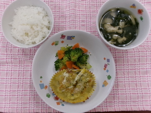 今日の給食の白ご飯・なかよしグラタン・ブロッコリーのおかか和え・ほうれん草のみそ汁がお皿に盛りつけられてい