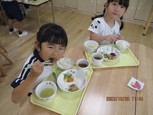 こどもたちがテーブルを囲んで大きな口開け食べている様子。