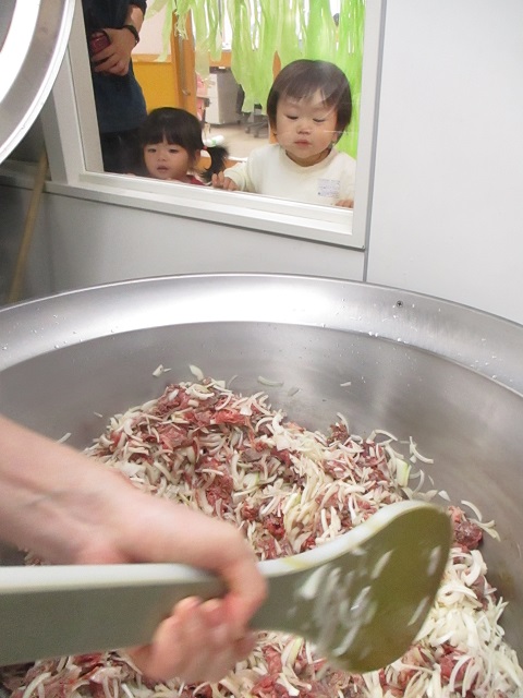 給食室の窓から回転釜の中のお肉をのぞくこども達