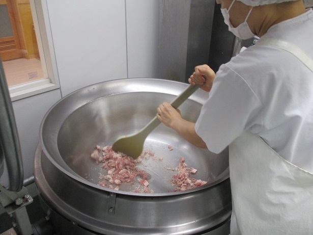回転窯で豚肉を調理員が炒めている。